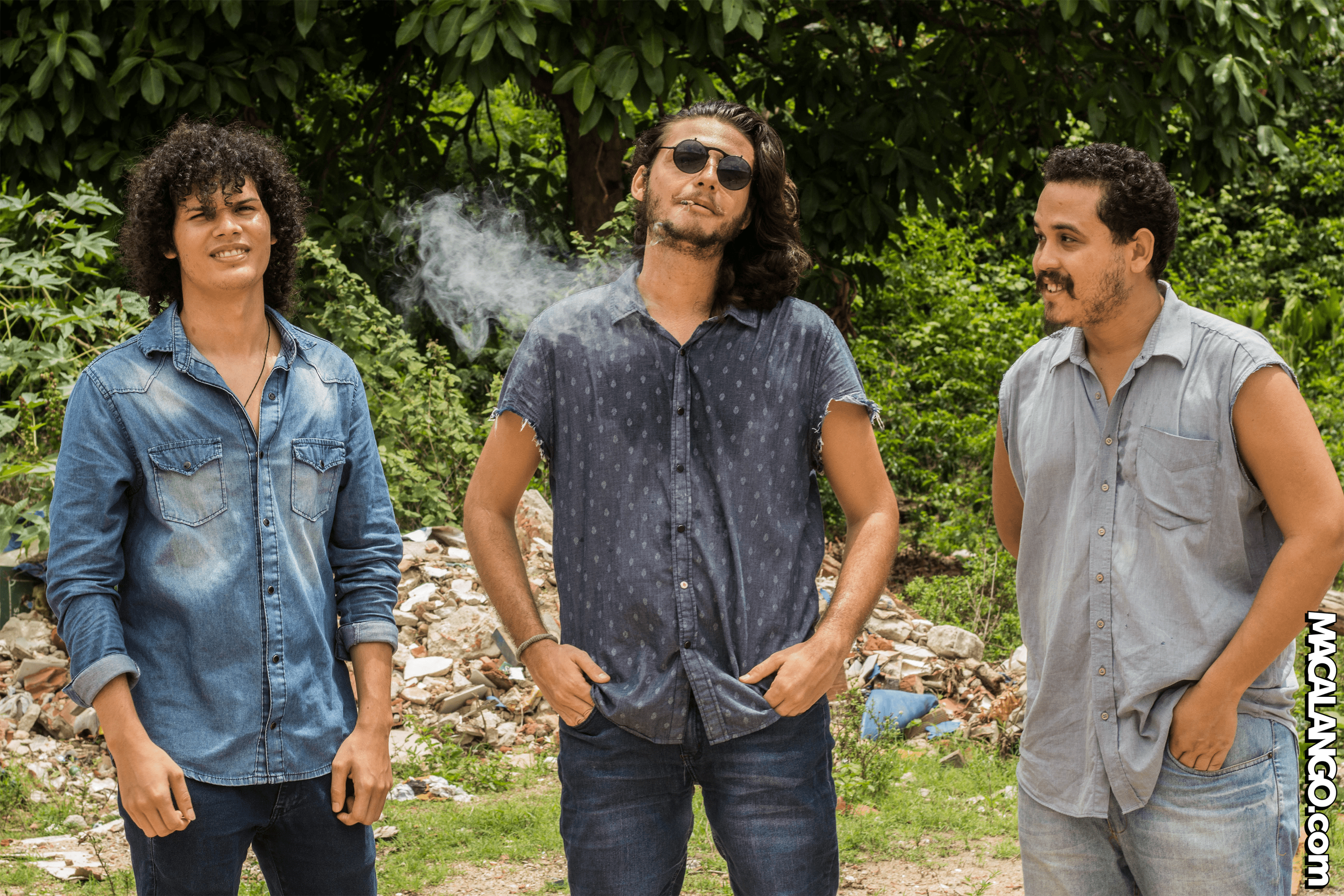 imagem da banda num terreno baldio cheio de plantas selvagens e concreto destruido. O vocalista está fumando um beck.