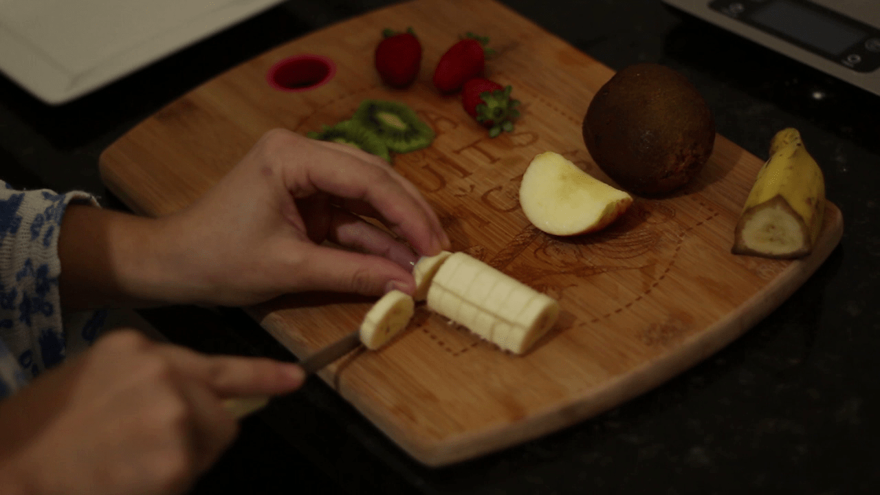 imagem da preparação da waffle, com kendi cortando kiwis, morangos, maçãs e bananas